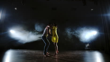 Zoom-camera-two-modern-ballet-dancers-are-dancing-on-stage-in-smoke-a-man-raises-his-partner-in-his-arms-and-rotates-in-the-air.-The-musical-uses-circus-acrobats-dancers.
